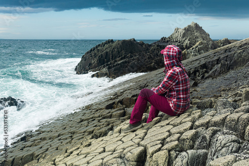 traveler sits on the shore of a stormy sea, on a natural pavement made of columnar granite photo