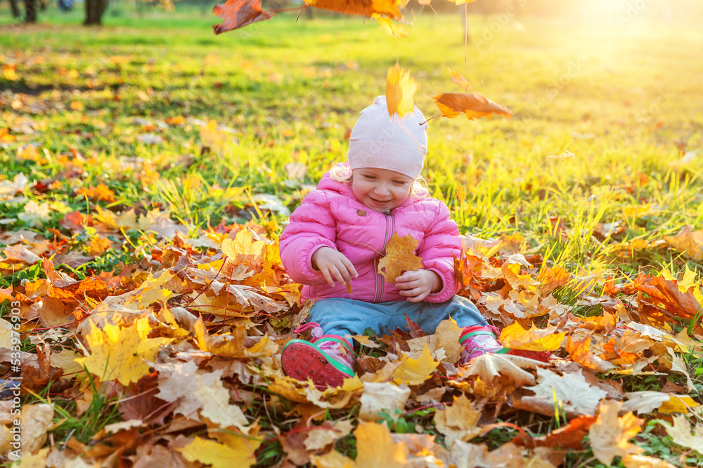 Happy young girl playing under falling yellow leaves in beautiful autumn park on nature walks outdoors. Little child throws up autumn orange maple leaves. Hello autumn concept Happy young girl playing under falling yellow leaves in beautiful autumn park on nature walks outdoors. Little child throws up autumn orange maple leaves. Hello autumn concept