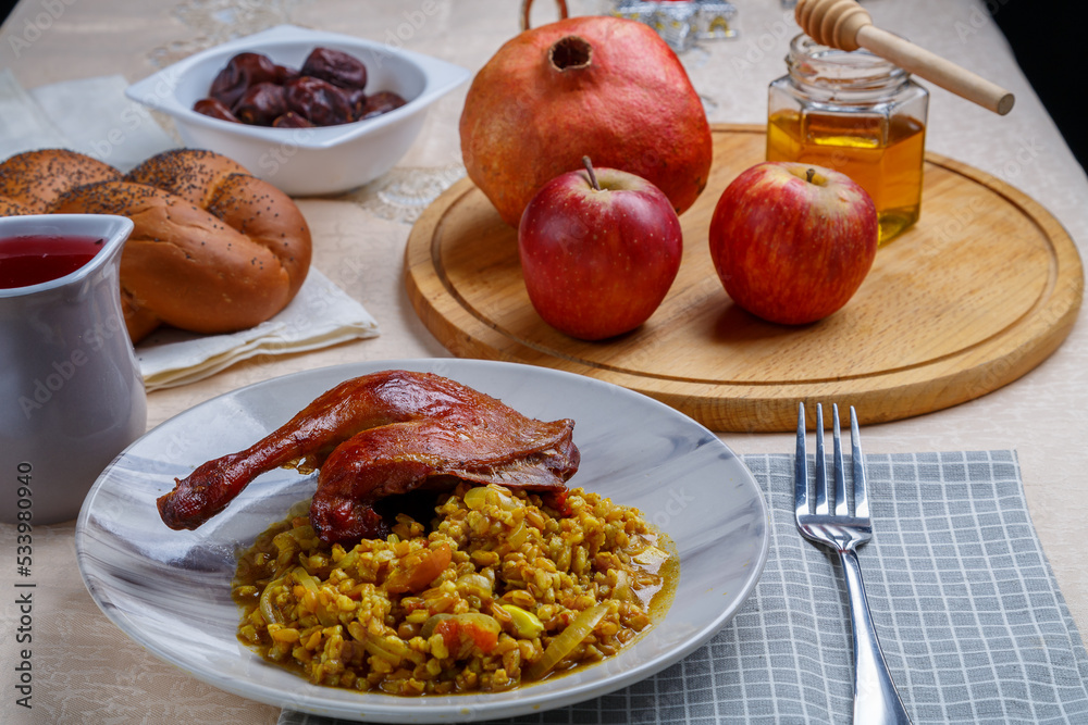 Honey, menorah apples and pomegranates and challah on the Rosh Hashanah table next to it in a plate of spelt with duck leg.