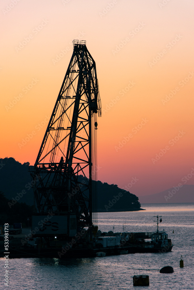 Silhouette of giant crane on Croatian Island at sunset with orange sky