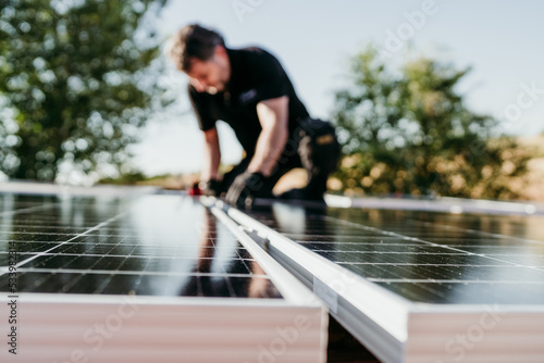 mature Technician man assembling solar panels on house roof for self consumption energy. Renewable energies and green energy concept. focus on foreground photo
