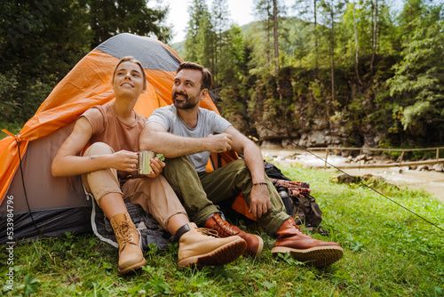 White young travelers resting in tents while hiking in green forest
