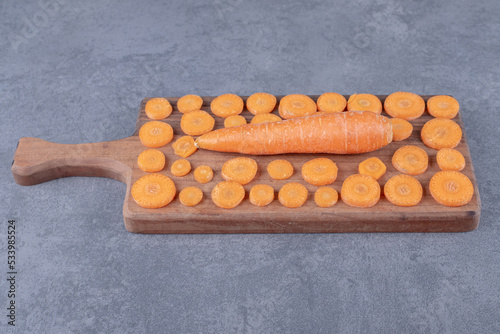 A wooden board of sliced and whole carrots , on the marble background photo