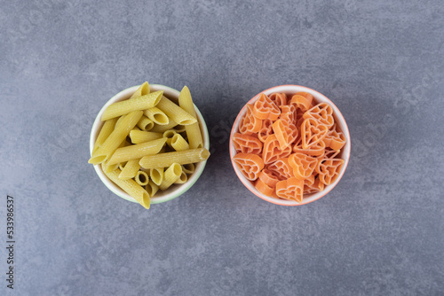 Two bowls of various pasta on stone background