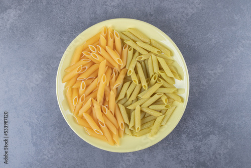 Raw green and yellow penne pasta on yellow plate