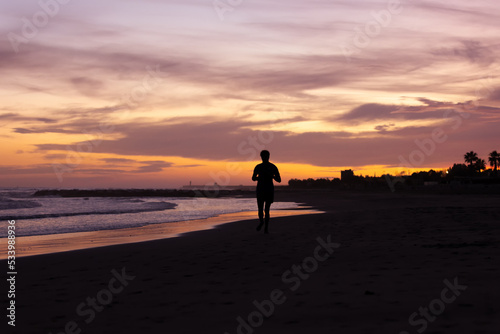 Silhouette of young fitness boy of a soccer team jogging, running at sunrise beach 