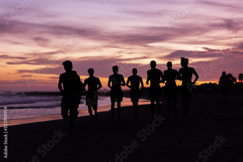 Silhouette of young fitness boy of a soccer team jogging, running at sunrise beach 