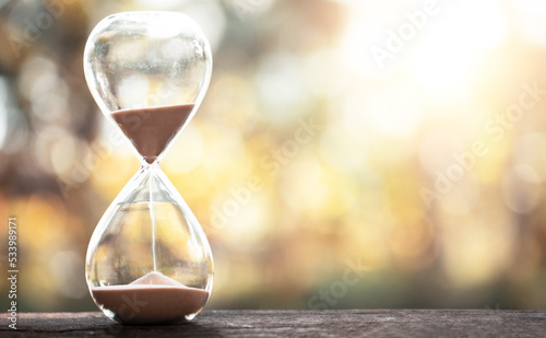 hourglass (sand clock) on an old wooden table with natural blur background, Hourglass as time passing concept for business deadline, Life-time passing concept, elapsed time concept, copy space