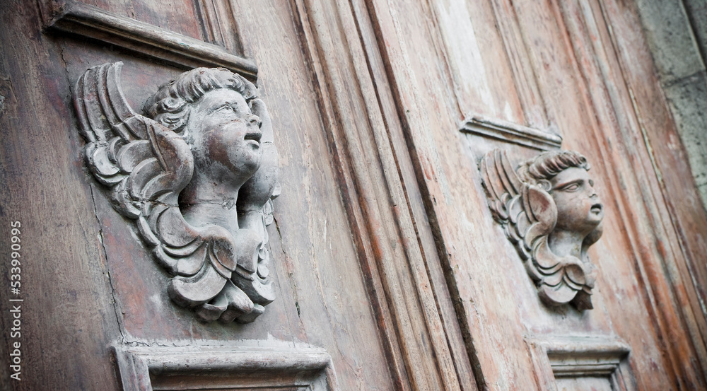 Sculpture of an old wooden angel against a wooden door of a church - more than 100 years old