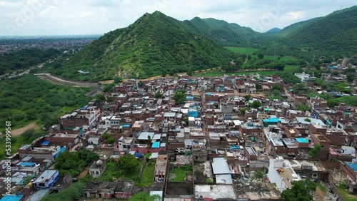 aerial drone shot flying over small village rural town with concrete and brick buildings with green tree covered aravalli mountains hills with clouds overhead near jaipur showing beautiful locations photo