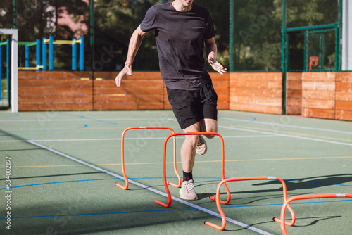 Blond boy in sportswear jumps over red obstacles to improve lower body dynamics. Plyometric training in an outdoor environment. Improve your skills