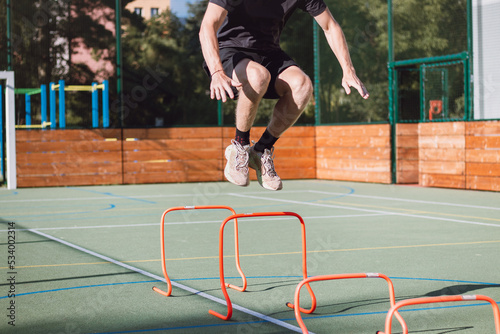 Blond boy in sportswear jumps over red obstacles to improve lower body dynamics. Plyometric training in an outdoor environment. Improve your skills