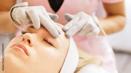 Beautician cosmetologist makes a procedure on the face with microcurrent therapy gloves. Hardware cosmetology in clinic salon for client. 