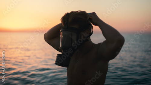 Silhouette of a boy putting on his gas mask at dawn in the ocean