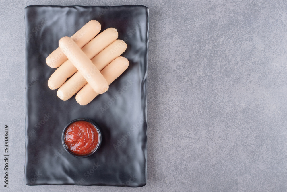 A black plate of boiled sausages with ketchup