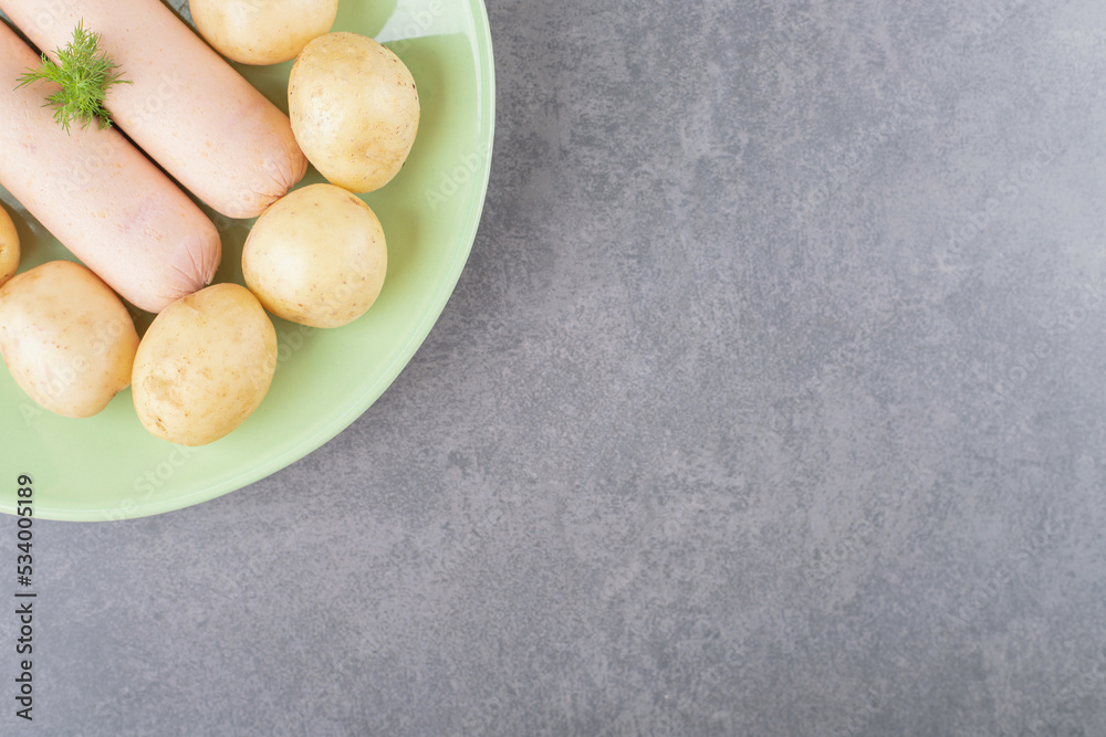 A green plate with boiled sausages and boiled potatoes A green plate with boiled sausages and boiled potatoes