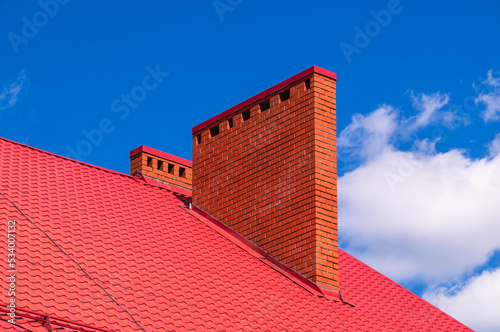 The pipe outside the house on the roof is made of red brick. Metal roof on the roof of the house. Metal tile sheets. The roofing material is made of sheet steel covered with a protective layer.