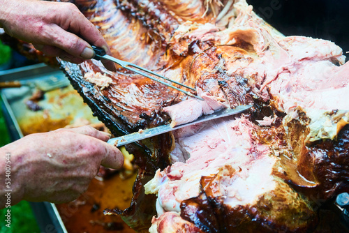 Chef Hands cutting whole grilled pork for steaks with knife. Pig grilled traditional coal and fire. The little piglet is roasted whole on an open fire. Pig on the spit
