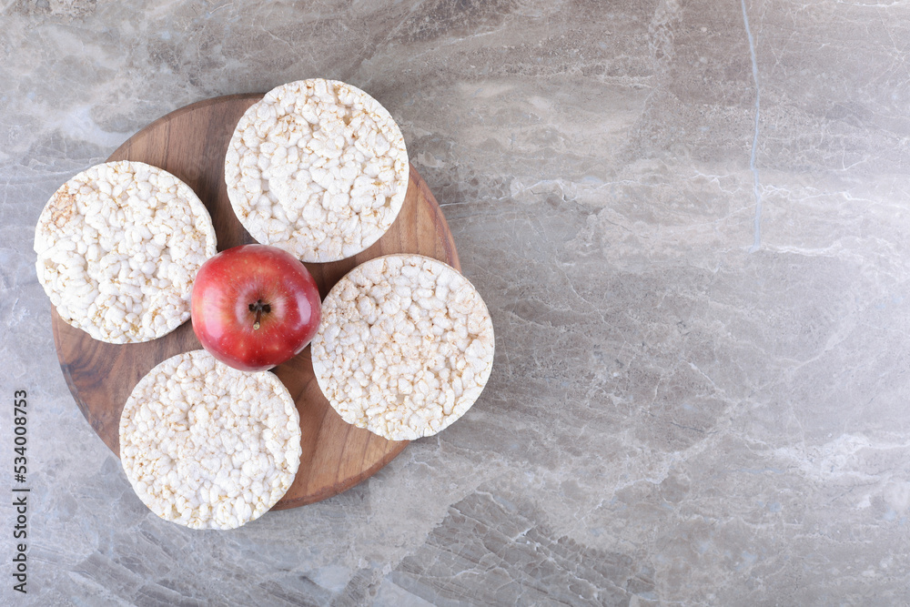 Apple and puffed rice cakes on the wooden tray, on the marble background Apple and puffed rice cakes on the wooden tray, on the marble background