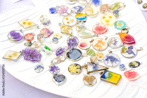 Epoxy resin jewelry - many handmade pendants with real flowers and plants inside on white stand. Making exclusive jewellery at home