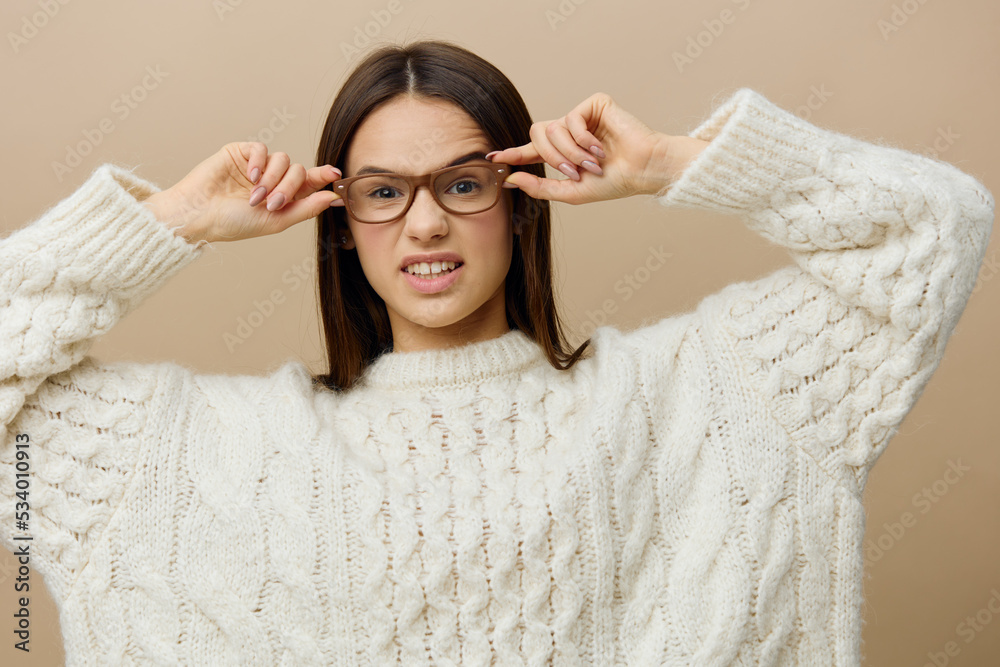 a funny, emotional woman stands on a light background in a large white sweater, wearing glasses slightly lowered, holding them with both hands and menacingly looking around with her elbows apart a funny, emotional woman stands on a light background in a large white sweater, wearing glasses slightly lowered, holding them with both hands and menacingly looking around with her elbows apart