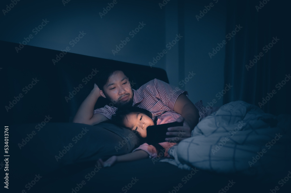 Dad and daughter sleep on the bed in bedroom,Watch cartoon with phone,Father day concept,Single dad,listen tale before sleep Dad and daughter sleep on the bed in bedroom,Watch cartoon with phone,Father day concept,Single dad,listen tale before sleep