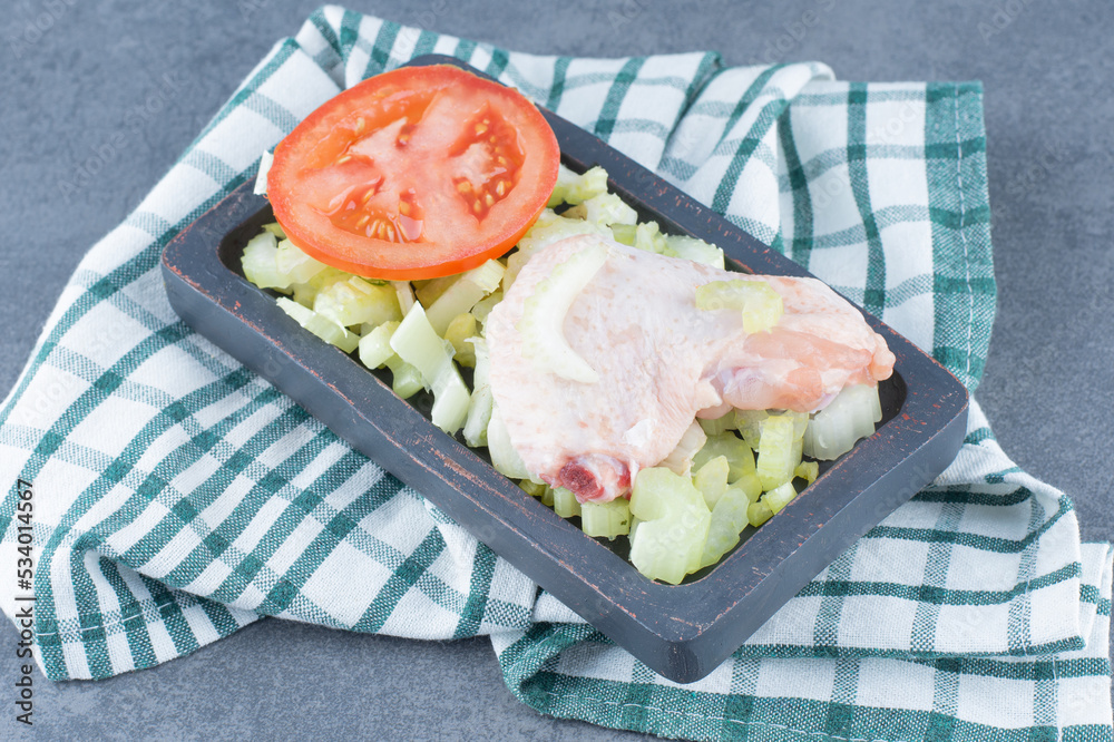 Uncooked chicken wings and tomato on black plate