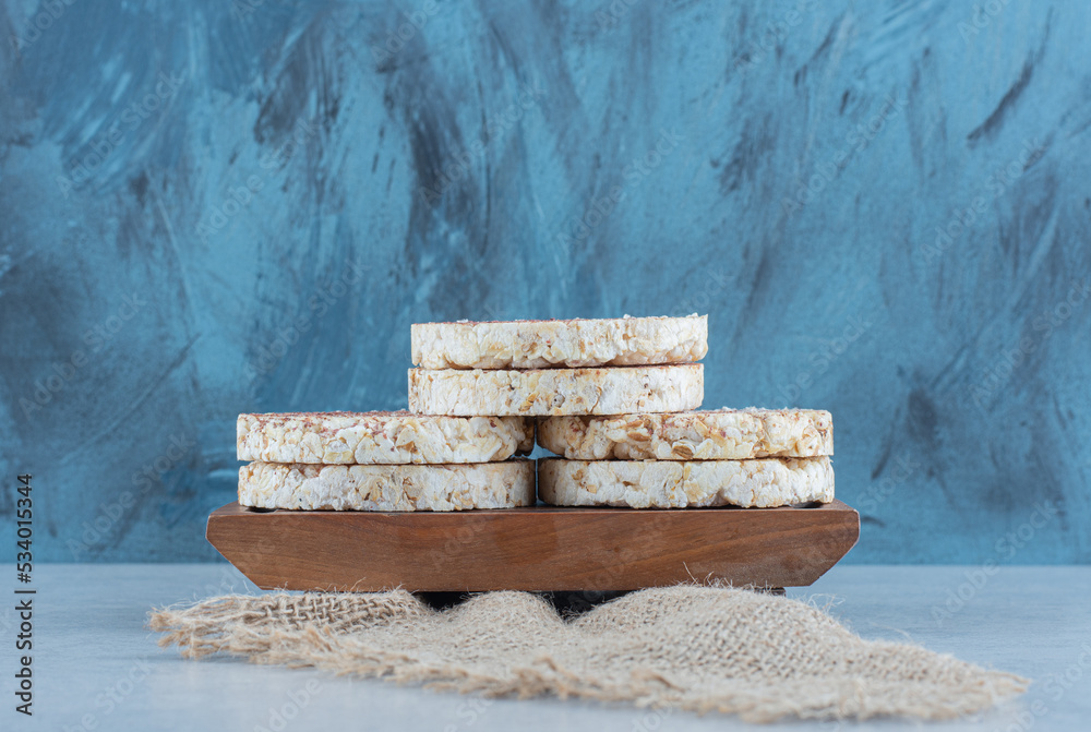 A pile of puffed rice cakes on the wooden tray on towel, on the marble background