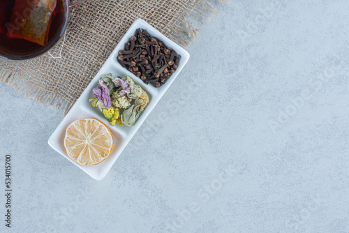 A cup of tea next to a bowl of dry sliced lemon and leaves on towel , on the marble background