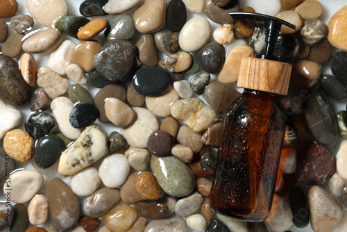 Bottle of cosmetic product on wet stones, top view. Space for text