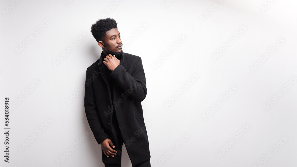 Serious young bearded guy in black clothes looking away while standing against white background Serious young bearded guy in black clothes looking away while standing against white background