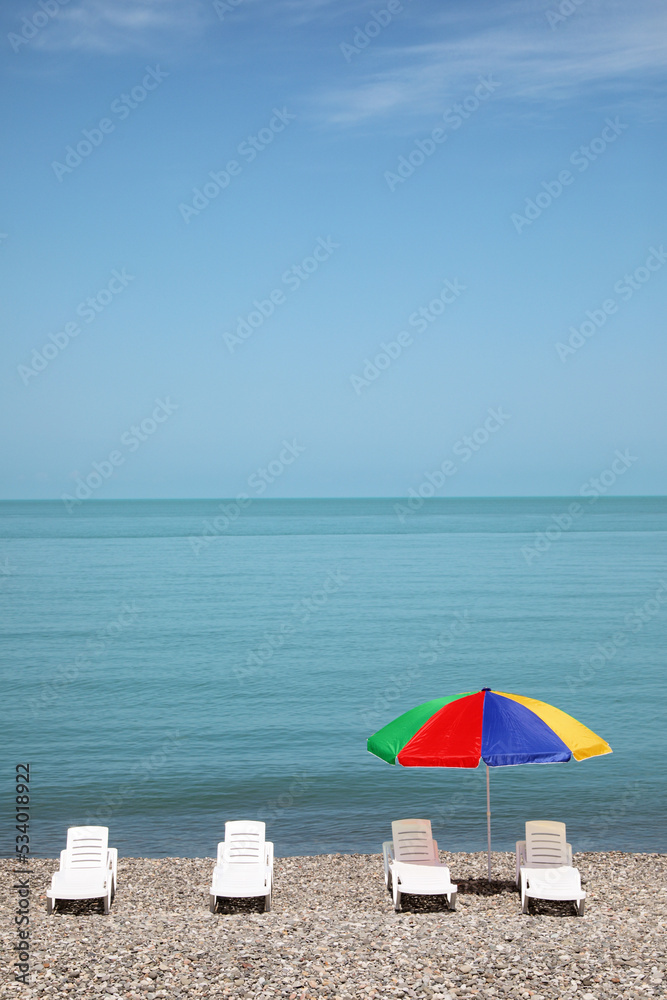 Beautiful view of umbrella and sunbeds on pebble beach near sea Beautiful view of umbrella and sunbeds on pebble beach near sea