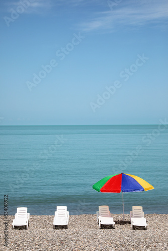 Beautiful view of umbrella and sunbeds on pebble beach near sea