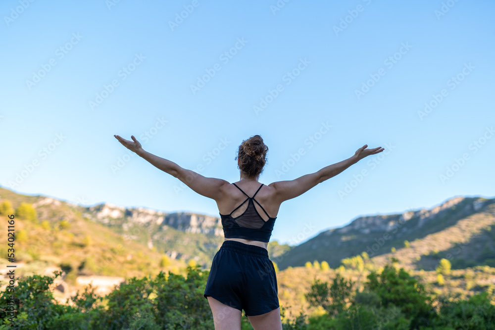 Caucasian woman breathing deeply on the mountain with open arms from behind Caucasian woman breathing deeply on the mountain with open arms from behind