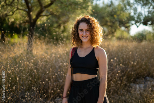 Happy caucasian woman with curly hair smiling in nature at golden hour