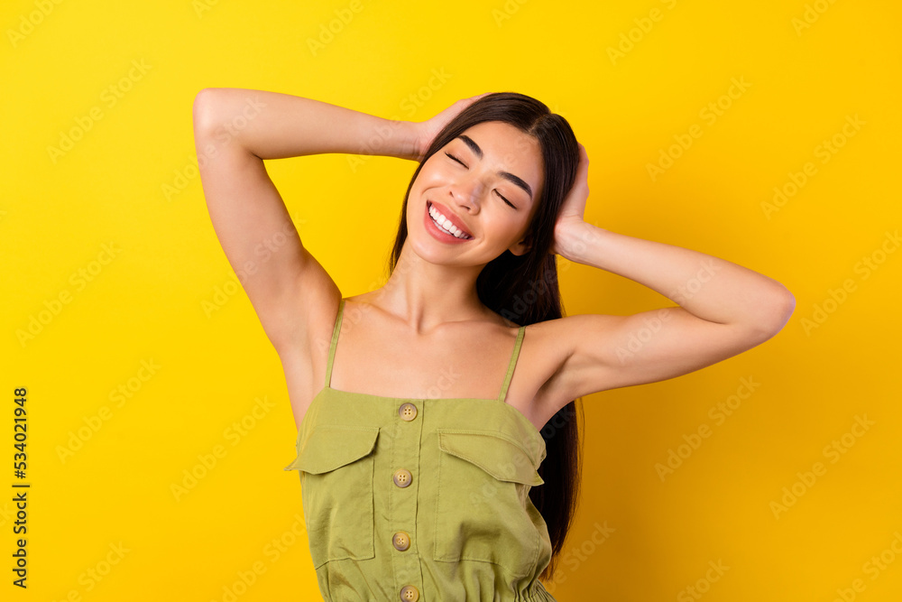 Photo of adorable sweet young lady wear green outfit arms head closed eyes isolated yellow color background Photo of adorable sweet young lady wear green outfit arms head closed eyes isolated yellow color background