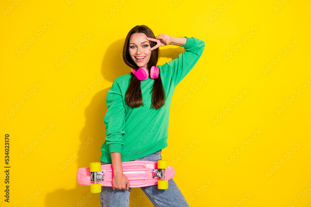 Portrait of cheerful excited lady hold skate hand fingers show v-sign near eye isolated on yellow color background Portrait of cheerful excited lady hold skate hand fingers show v-sign near eye isolated on yellow color background