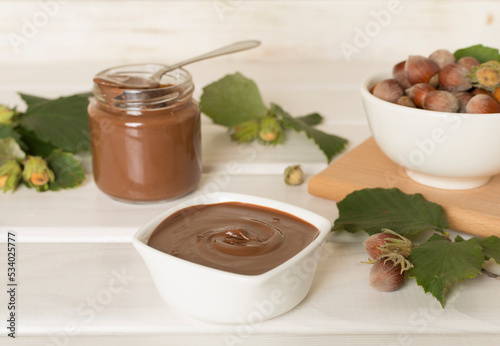 Hazelnut cream with nuts and green leaves on wooden table