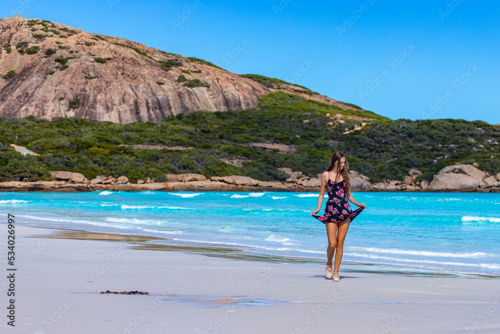 a long-haired girl in a black dress with roses dances on a paradise beach with white sand and turquoise water and orange rocks, cape le grand national park near esperance, western australia
