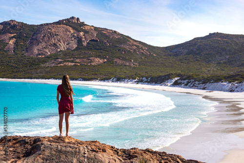 a long-haired girl in a dress walks along a paradise beach with white sand and turquoise water and orange rocks, cape le grand national park near esperance, western australia