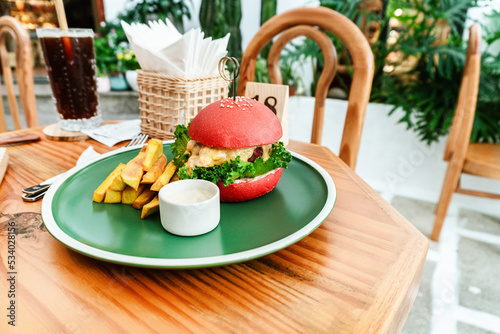 Vegan burger, in a red bun, dish with chips, on a green plate, on a wooden table, healthy vegetarian food.