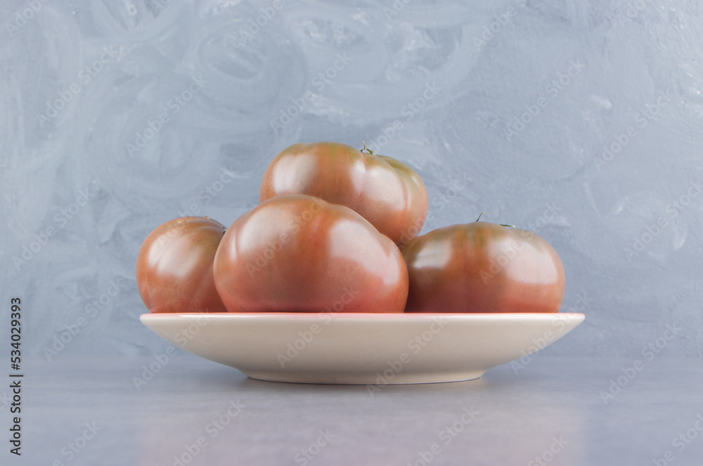 Appetizing tomatoes in the plate , on the marble background Appetizing tomatoes in the plate , on the marble background
