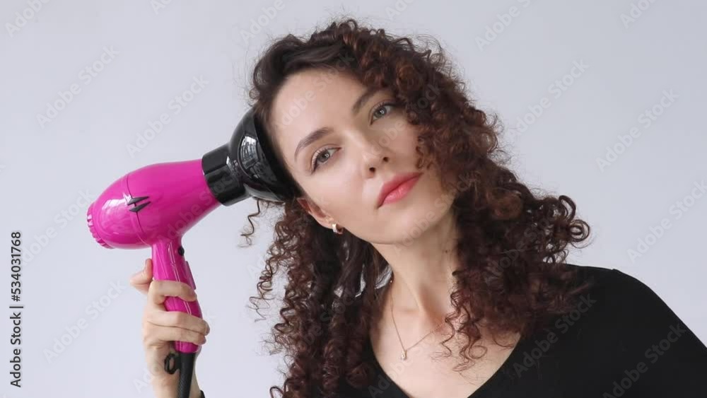 Woman gives herself a curly hairstyle. Hair care concept. A curly woman dries her hair at home with a hair dryer with a diffuser attachment. A beautiful girl uses a modern hair dryer.