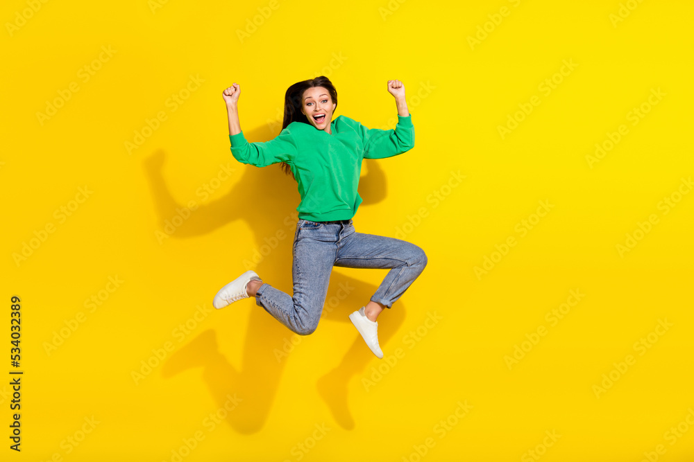 Full size photo of sporty young lady jumping raise fists marathon winner wear stylish green sportswear isolated on yellow color background