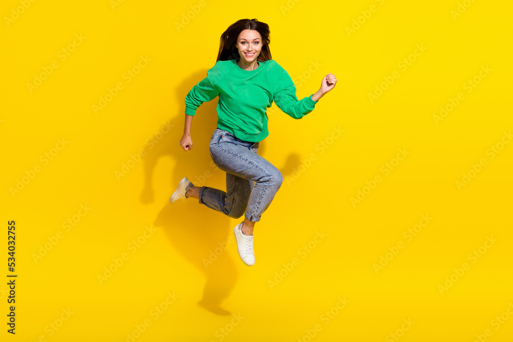 Full size photo of cute young unstoppable woman smile running marathon dressed trendy green sweatshirt isolated on yellow color background Full size photo of cute young unstoppable woman smile running marathon dressed trendy green sweatshirt isolated on yellow color background