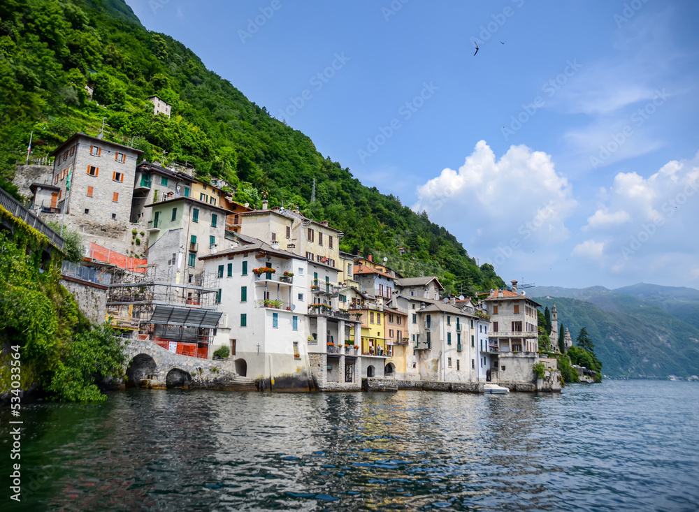 Waterfront colorful houses in Lake Como in Italy with green mountain behind. Authentic rural town in lake shore famous for summer vacation and tourist attraction. Beautiful panorama