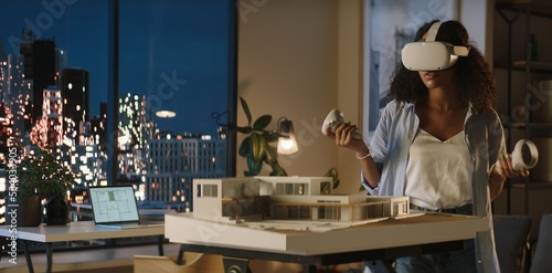 Portrait of African American female architect or student using a virtual reality VR headset to work on a house project late at night, preparing for presentation with a client