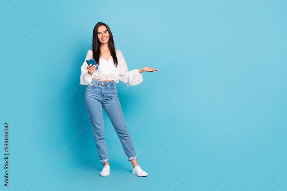 Full length portrait of attractive cheerful person hold telephone arm demonstrate empty space isolated on blue color background