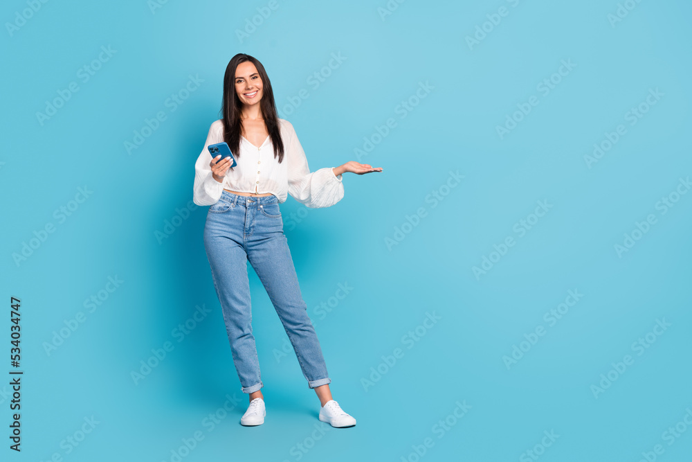 Full length portrait of attractive cheerful person hold telephone arm demonstrate empty space isolated on blue color background Full length portrait of attractive cheerful person hold telephone arm demonstrate empty space isolated on blue color background