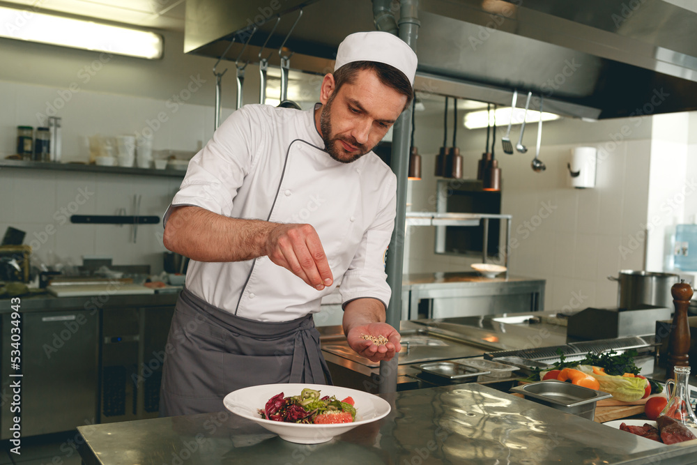 Chef sprinkles salt to salad of fresh vegetables in kitchen of restaurant. Tasty and healthy food Chef sprinkles salt to salad of fresh vegetables in kitchen of restaurant. Tasty and healthy food